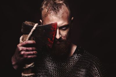 Portrait of man holding axe against face over black background