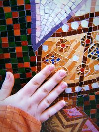 Cropped image of person hand against multi colored tiled floor