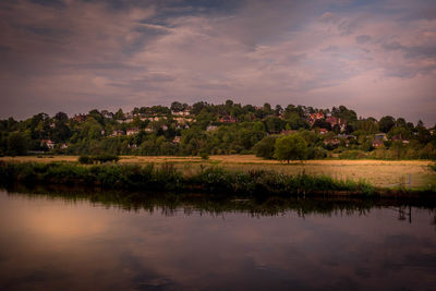 Scenic view of lake by trees and buildings against sky