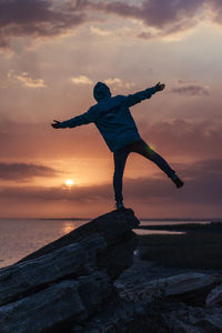 Man standing on rock by sea against sky during sunset