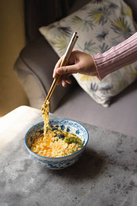 Cropped hand of woman eating noodles on table at home