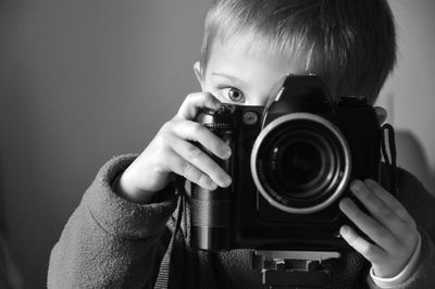 Close-up portrait of boy photographing with camera by wall