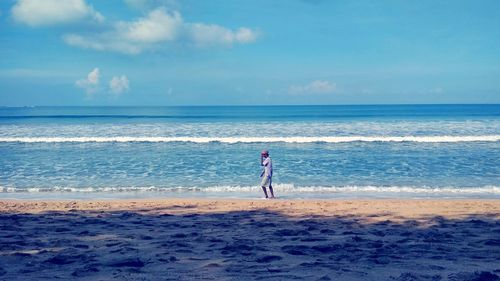 Side view of man walking at beach against blue sky