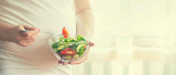 Midsection of pregnant woman with bowl of salad