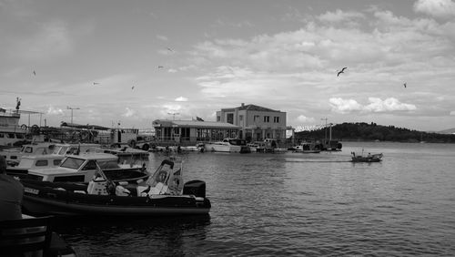 Boats moored at harbor against sky in city