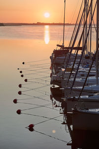 Sailboats moored on sea against sky during sunset