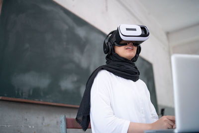 Low angle view of young woman looking through virtual reality simulator in classroom
