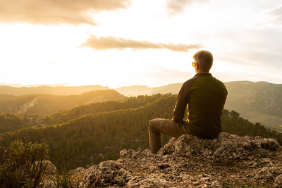 Rear view of man sitting on mountain against sky