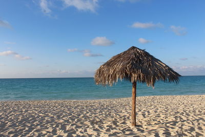 Thatched roof at beach against sky during sunny day