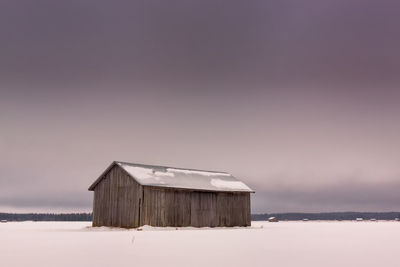 Barn on snowy landscape against sky