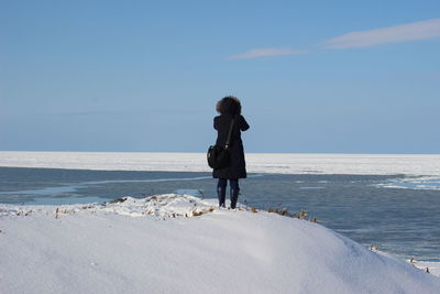 Rear view of woman standing on beach against sky