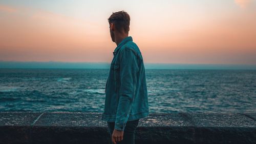 Man looking at sea against sky during sunset