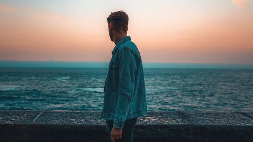 Side view of man looking at sea against sky during sunset