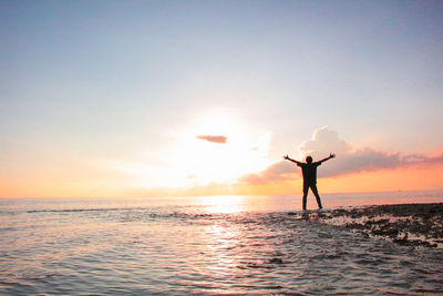 Silhouette person standing in sea against sky during sunset