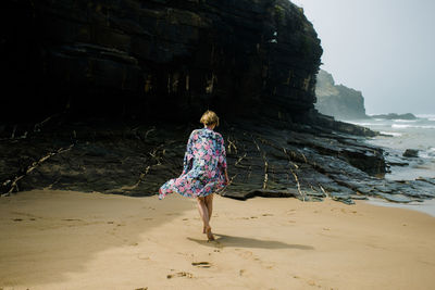 Rear view of young woman walking at beach against rock formation