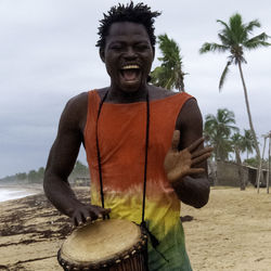 Portrait of young man standing by palm tree on beach