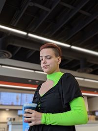 Low angle portrait of woman holding drink while standing in cafe