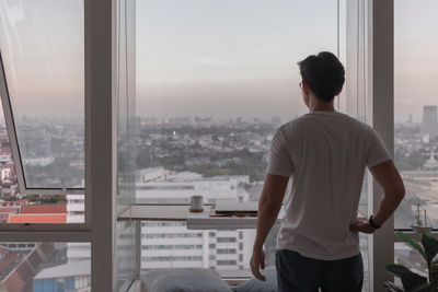 Rear view of man looking through cityscape window