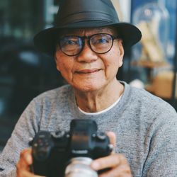Portrait of senior man holding camera while sitting in cafe