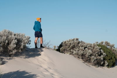 Rear view of man standing on beach against clear sky