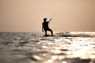 Silhouette man wakeboarding in sea against sky during sunset