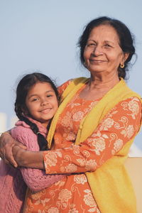 Portrait of smiling mother embracing daughter against clear sky