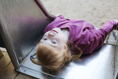 Girl with red hair lying on slide at playground