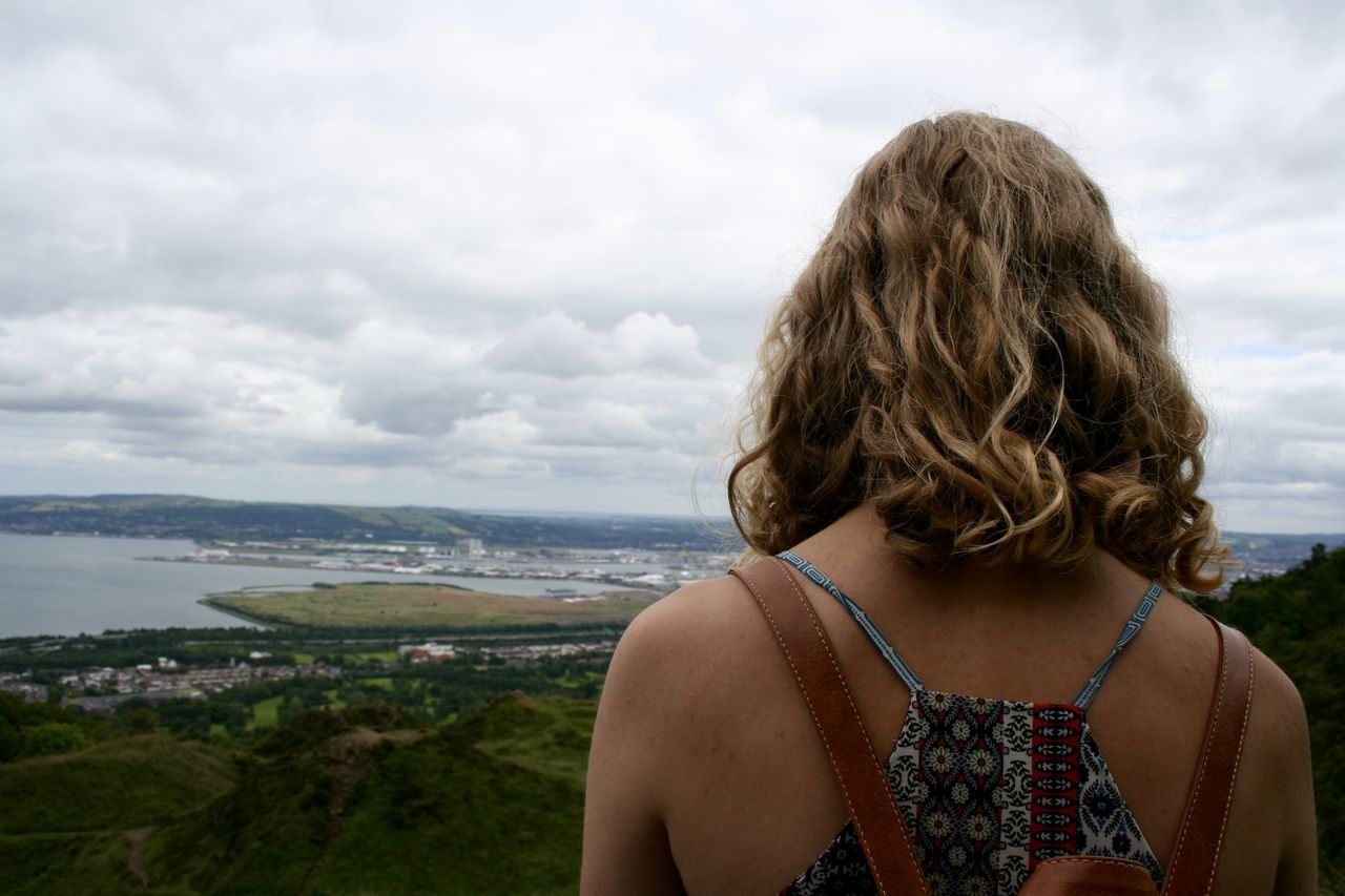 sky, lifestyles, leisure activity, sea, long hair, cloud - sky, water, cloudy, cloud, scenics, nature, brown hair, horizon over water, tranquil scene, beauty in nature, tranquility, headshot, casual clothing, vacations, looking at view, day, relaxation, outdoors, tourist, mountain