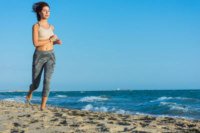 Full length of woman standing on beach against clear blue sky