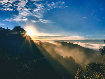 Sunlight streaming through clouds over landscape during sunset