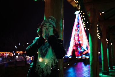 Man standing on illuminated christmas tree during winter at night