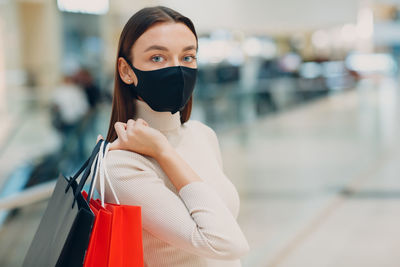 Portrait of woman wearing mask holding shopping bags outdoors