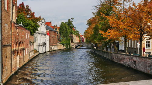 Canal amidst buildings against sky during autumn