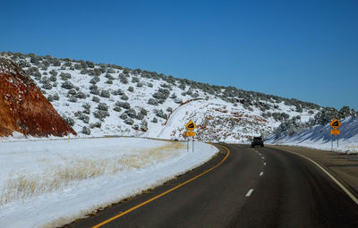 Road amidst snowcapped mountains against clear sky