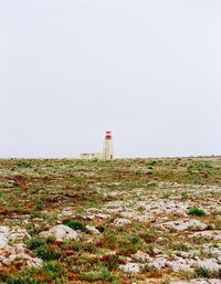 Lighthouse on field by building against clear sky