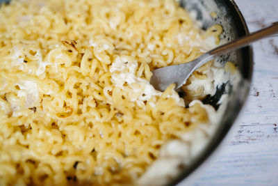 Classic homemade macaroni and cheddar cheese on black plate with a fork on white wooden table.