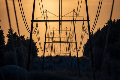 Silhouette trees and electricity pylon against sky at sunset