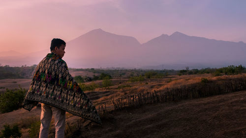 Man standing on field against mountain during sunset