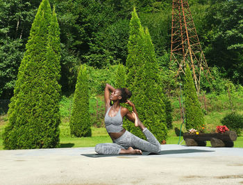 Side view of woman sitting on plant against trees