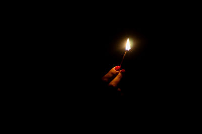 Close-up of hand holding lit matchstick in darkroom