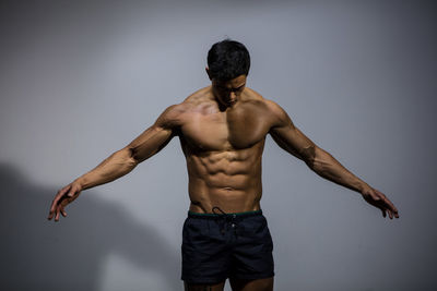 Shirtless muscular man standing against gray background