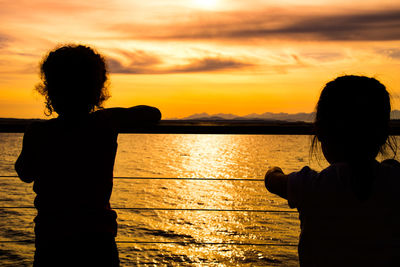 Rear view of silhouette girls looking at sea view during sunset