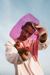 Midsection of woman holding pink flower against sky