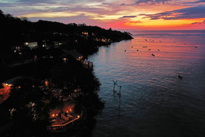 High angle view of illuminated city by sea against sky during sunset