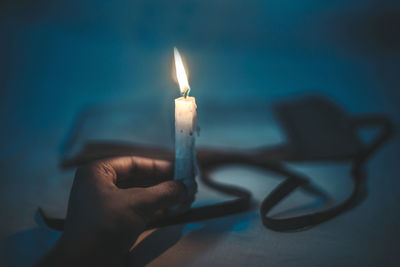 Cropped hand holding lit candle in darkroom