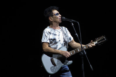 Full length of man playing guitar against black background