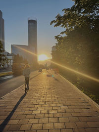 People walking on footpath in city against sky at sunset