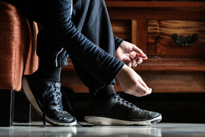 Low section of woman tying shoelace at home