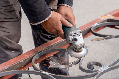 Man grinds metal with angle grinder in metal workshop. sparks fly on the sides. 
