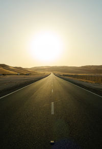 Empty road along landscape at sunset